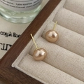Makroaufnahme eleganter champagnegoldener Perlenohrringe auf einem Schmuckdisplay aus Holz - Goldene ovale Perlenohrringe