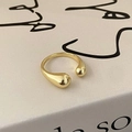 Close-up of minimalist gold crossover ring with teardrop ends on a textured book page - Ball Style / Gold