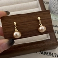 Primer plano de elegantes pendientes de perlas rosa en forma de gota con base dorada - Pendientes colgantes de perlas ovales con pasador de bola dorado