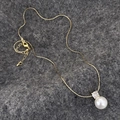Dettaglio della collana con pendente di perla dorata e zircone su sfondo grigio scuro - Oro Zirconia Perla Bianca