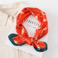 Détail macro d'un foulard en soie rouge à motif flamant posé sur une chemise beige - Orange