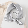 Close-up of knotted silver silk square scarf with glossy satin finish on beige fabric - Light Gray