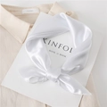 Detailed view of elegant white satin square scarf tied in a bow on a fashion magazine - White