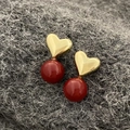 Macro detail of red pearl heart earrings with gold finish on dark wool texture - Red Pearl Gold Heart Earrings