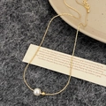 Detalle de un collar de cadena de oro con colgante de perla blanca sobre fondo fieltro - Collar de Oro