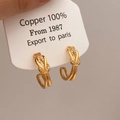 Makro-Detail von goldenen Knoten-Ohrringen mit Zirkonia und Kupfer-Materialetikett - Gold