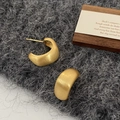 Detail van mat geborstelde gouden oorbellen met breed boogontwerp op grijze textuur - Goud