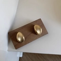 Detail of matte gold irregular pebble earrings with brushed texture on walnut wood - Gold Brushed Style