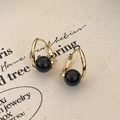 Macro detail of U-shaped gold earrings with black polished beads on linen texture - Black Agate