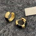 Detail von goldenen Creolen mit schwarzer Emaille auf grauem strukturiertem Hintergrund - Schwarze Tropföl-Ohrringe