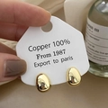 Gros plan sur des boucles d'oreilles galets dorées polies en cuivre sur leur support - Doré
