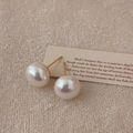Detalle de pendientes de perlas redondas con brillo irisado sobre un fondo textil cálido - 12mm