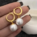 Detailed view of large white pearls and matte gold 18k plated hoops held by hand - Gold Small Pearl Earrings