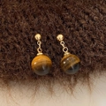Close-up of natural tiger eye stone bead earrings on a brown textured fabric background - Gold
