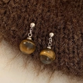 Macro shot of natural tiger eye stone earrings on a dark brown plush textured fabric - Silver