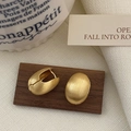Dettaglio macro di orecchini ovali in oro spazzolato opaco su espositore in legno - Oro