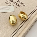 Dettaglio macro di orecchini ovali dorati a forma di guscio su un libro vintage - Cerchio Ovale / Oro