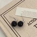 Macro view of minimalist black pearl drop earrings with silver hooks on vintage paper - Silver Black Pearl Hook