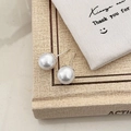 Detailed close-up of classic round white pearl stud earrings on a textured beige surface - 10mm Shell Pearl Stud