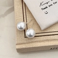 Detailed view of large white pearl earrings placed on a vintage book with soft lighting - 12mm Shell Pearl Stud