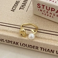 Détail d'une bague ouverte dorée avec perle d'eau douce sur un livre rétro texturé - Bague Géométrique Perle d'Eau Douce / Doré