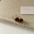 Dettaglio di orecchini a lobo rotondi in smalto marrone scuro con perni dorati su trama - 10mm Cioccolato