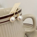 Detalle de pendientes de perlas colgando de una taza de cerámica vintage con ganchos oro - Pendientes de Perlas Mabe Dorados