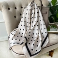 Close-up of silk-feel polka dot scarf draped over a beige armchair and leather handbag - 90x90cm / Beige