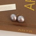 Makroaufnahme von grauen Perlenohrsteckern mit Goldstiften auf einer eleganten Geschenkbox - Dunkelgrau
