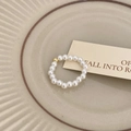 Nahaufnahme eines minimalistischen Süßwasserperlen-Rings mit Goldperle auf Keramik - Elastischer Perlenstil / Goldperle Perle