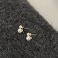 Detalle de pendientes de doble perla dorados sobre un fondo de tela de lana con textura - Estilo Dorado / Blanco