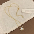 Detalle de un colgante de herradura dorado con perla sobre un fondo de tela suave y elegante - Collar de Oro Con Perla Blanca