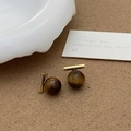 Détail de boucles d'oreilles en œil de tigre avec tiges dorées sur surface texturée - Clous d'Oreilles Barre Oeil de Tigre Doré