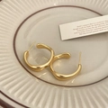 Vista macro de pendientes de aro dorados con diseño ondulado sobre una bandeja de cerámica - Dorado