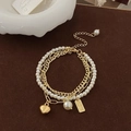 Detailed macro of a triple-layered gold pearl bracelet with heart and tag pendants - Heart Three-layer Bracelet (Gold Plated)