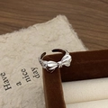 Close-up of polished silver bow ring resting on a velvet jewelry box and wooden desk - Bowknot Open Style / Silver