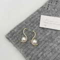 Detailed view of S-curve gold earrings with zircon and white pearls on gray fabric - Gold S-Shape Micro-Inlaid Style / Gold