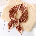 Gros plan d'un foulard en soie fleuri noué avec des bordures roses sur fond texturé - 90x10cm / Bordure Café Khaki Florale