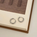 Primo piano di orecchini a cerchio in argento lucido su un libro aperto stile minimal - Argento