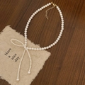 Detail of white pearl necklace featuring a pearl-studded bow and gold lobster clasp - 6mm Pearl Bow Knot Necklace