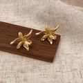 Vue détaillée de boucles d'oreilles fleurs dorées mates sur un support en bois brun - Or (Plaqué Or Véritable)