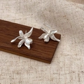 Gros plan de boucles d'oreilles fleur argent mat avec pétales texturés sur bois - Argent (Plaqué Argent Épais)