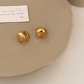 Orecchini a semisfera in oro lucido presentati su un piatto di ceramica minimal - Oro
