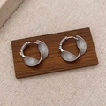 Detail view of silver twisted hoop earrings with snakeskin texture on a wooden block - Silver Twisted Mobius Hoop Earrings