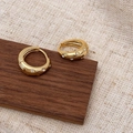 Dettaglio di orecchini a cerchio dorati con zirconi su espositore in legno - Oro