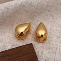 Detailopname van gepolijste gouden druppeloorbellen op linnen en hout decor - Gouden Druppel Oorbellen (Echt Verguld)