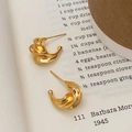 Dettaglio di orecchini a cerchio dorati ritorti con trama irregolare su pagina vintage - Oro
