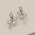 Dettaglio orecchini a fiocco d'argento con perla su superficie bianca minimalista - Orecchini di Perle con Fiocco / Argento