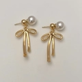 Détail de boucles d'oreilles nœud doré avec perles élégantes sur fond minimaliste - Boucles d'Oreilles Nœud Doré Brillant Perle Blanche