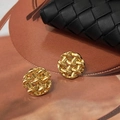 Dettaglio degli orecchini a perno intrecciati dorati con trama geometrica su pelle marrone - Oro